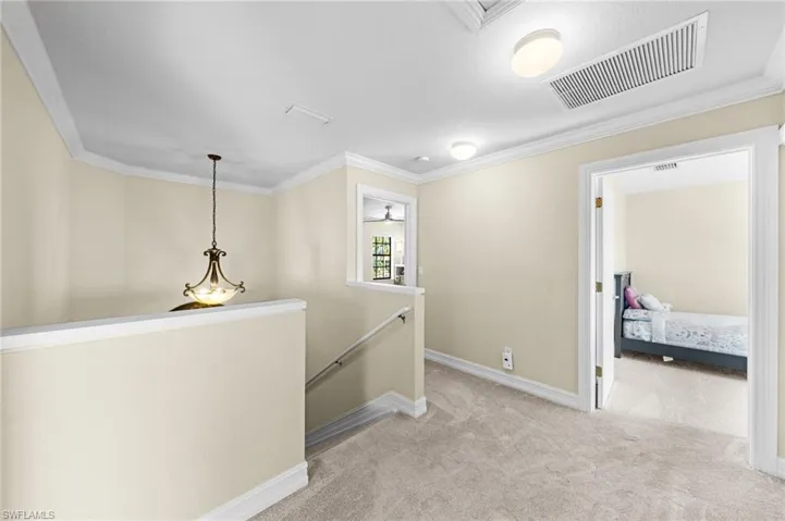 Hallway with an upstairs landing, light carpet, and crown molding