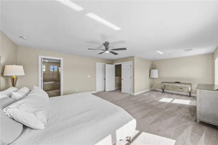 Bedroom with light colored carpet, ceiling fan, and connected bathroom