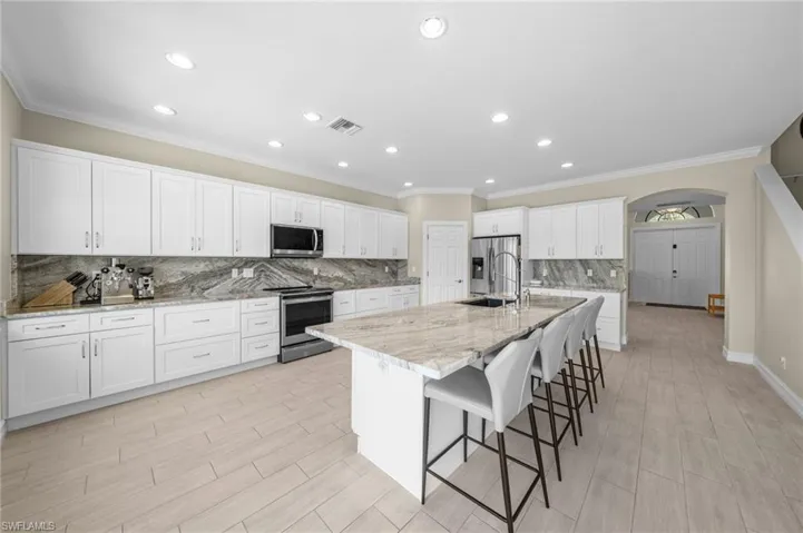 Kitchen featuring ornamental molding, white cabinets, a kitchen breakfast bar, decorative backsplash, and stainless steel appliances