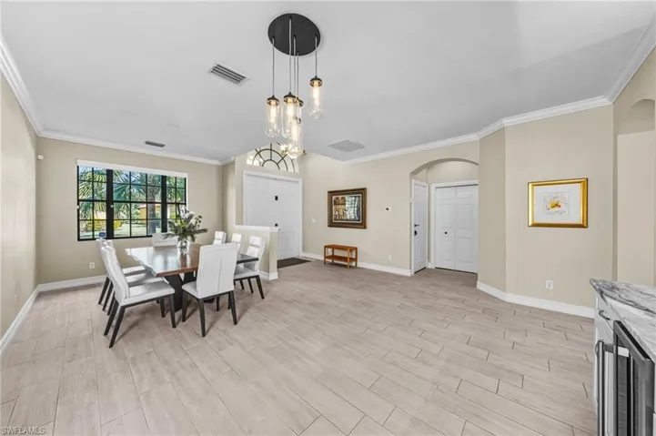 Dining area featuring beverage cooler, ornamental molding, arched walkways, wood tiled floors, and a chandelier