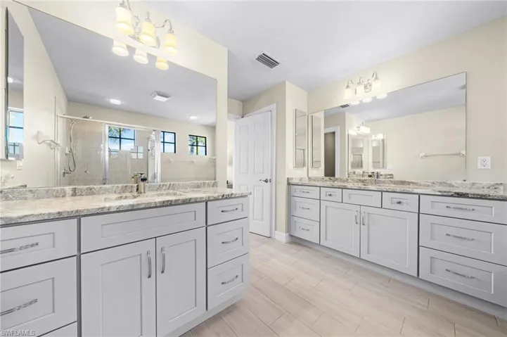 Bathroom featuring a stall shower, two vanities, a chandelier, and wood finish floors