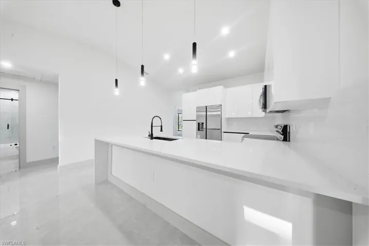 Kitchen featuring a peninsula, stainless steel appliances, white cabinetry, and light stone counters