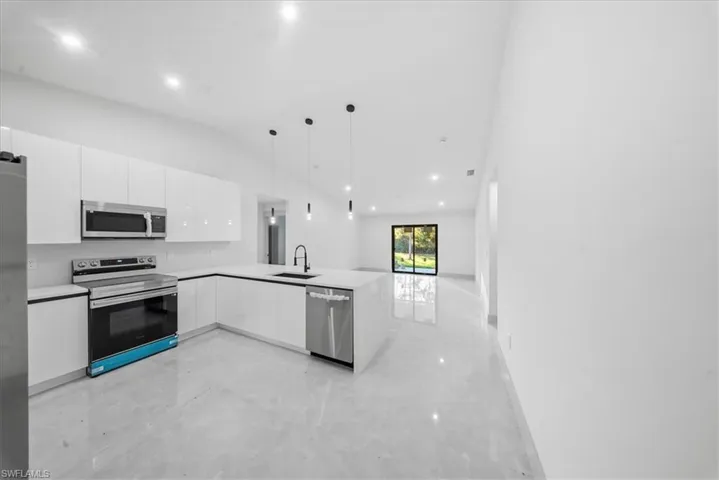 Kitchen with stainless steel appliances, white cabinetry, a peninsula, hanging light fixtures, and vaulted ceiling
