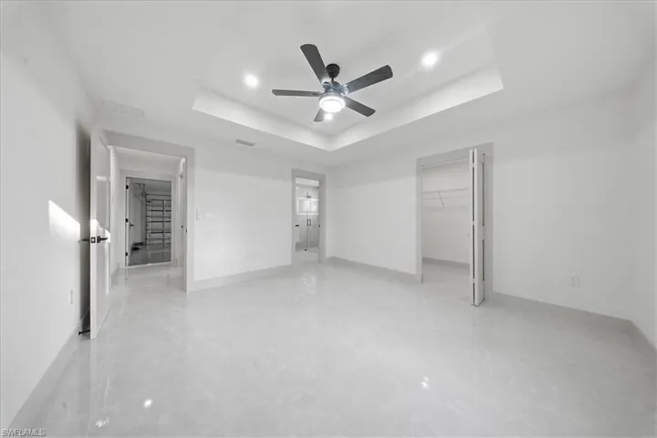Unfurnished bedroom with a walk in closet, a ceiling fan, and a tray ceiling