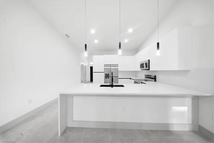 Kitchen featuring a peninsula, white cabinetry, stainless steel appliances, light stone countertops, and modern cabinets
