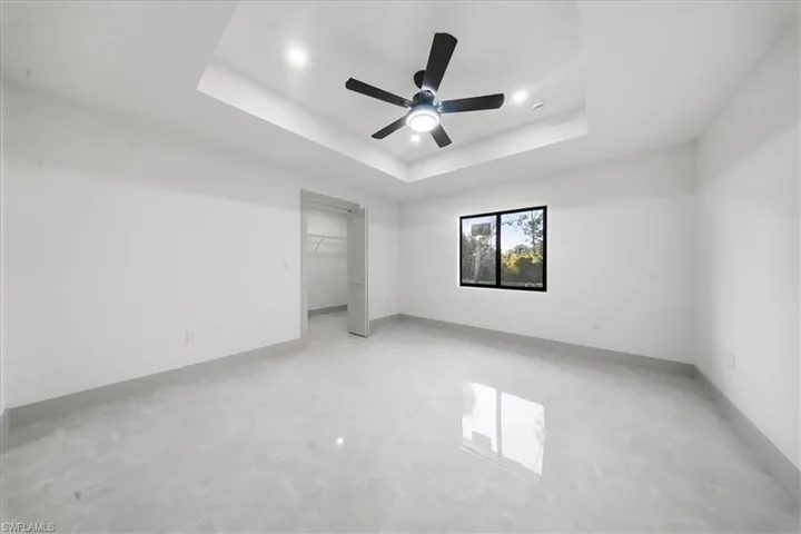 Unfurnished bedroom with a ceiling fan, a walk in closet, a raised ceiling, and concrete floors