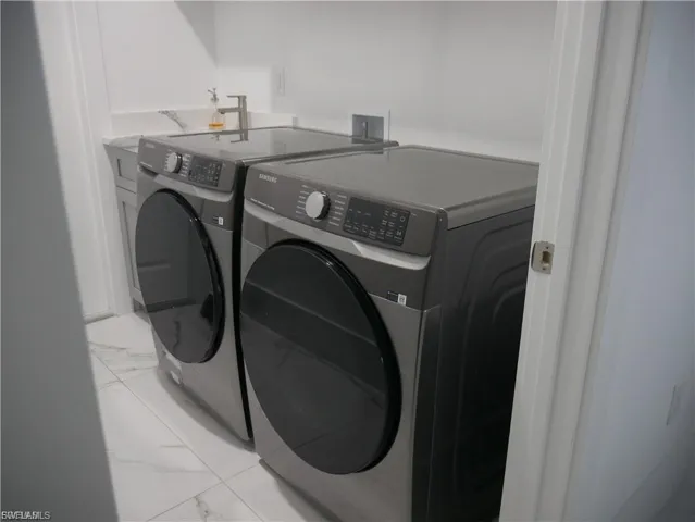 Laundry area with light marble finish flooring and washing machine and clothes dryer