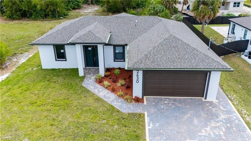 Single story home featuring a front lawn, decorative driveway, a garage, roof with shingles, and stucco siding