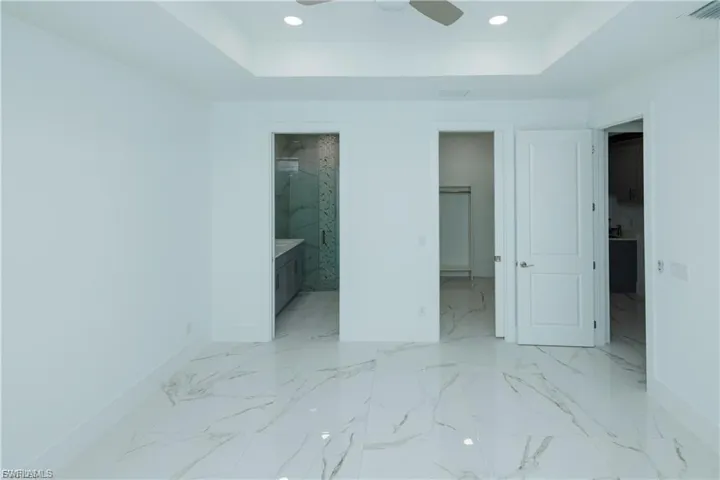 Unfurnished bedroom with a walk in closet, a tray ceiling, recessed lighting, connected bathroom, and light marble finish flooring