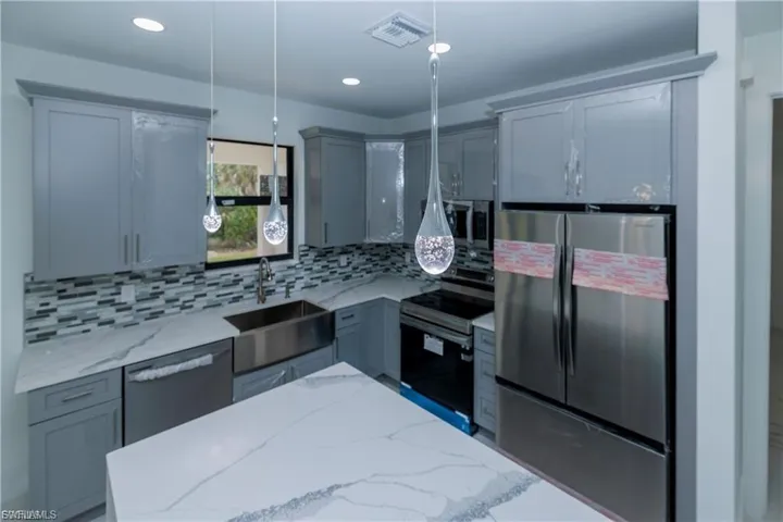 Kitchen featuring appliances with stainless steel finishes, gray cabinetry, light stone counters, backsplash, and hanging light fixtures