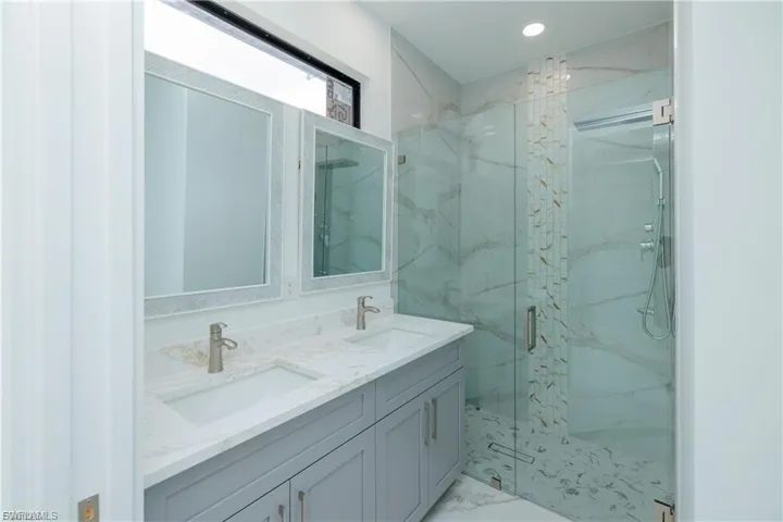 Bathroom featuring double vanity, a marble finish shower, light marble finish flooring, and recessed lighting