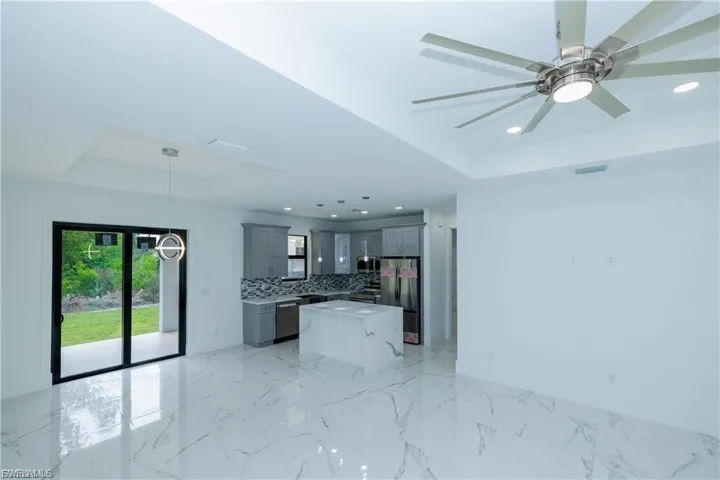 Unfurnished living room featuring a tray ceiling, light marble finish flooring, recessed lighting, and a ceiling fan