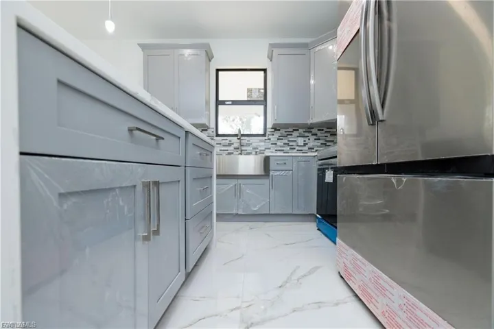 Kitchen featuring freestanding refrigerator, light marble finish floors, gray cabinets, black range, and light countertops