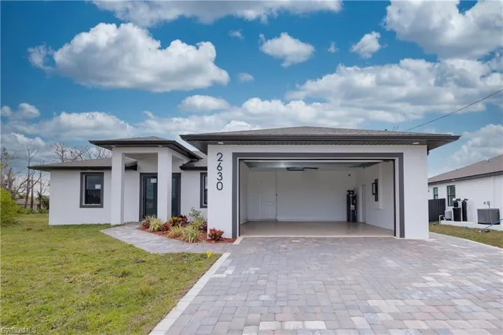 Prairie-style home featuring a front yard, decorative driveway, stucco siding, and an attached garage