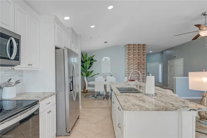 Kitchen featuring white cabinets, appliances with stainless steel finishes, light stone countertops, backsplash, and recessed lighting