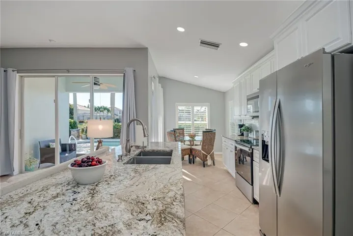 Kitchen featuring stainless steel appliances, white cabinets, vaulted ceiling, light stone counters, and recessed lighting