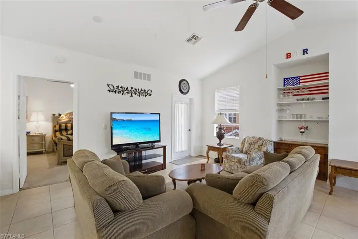 Living room featuring lofted ceiling, light tile patterned floors, and a ceiling fan