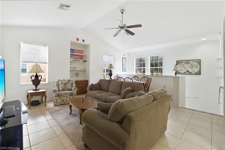 Living room with light tile patterned floors, ceiling fan, and lofted ceiling