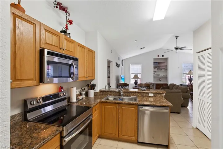 Kitchen with stainless steel appliances, light tile patterned floors, a peninsula, lofted ceiling, and a ceiling fan