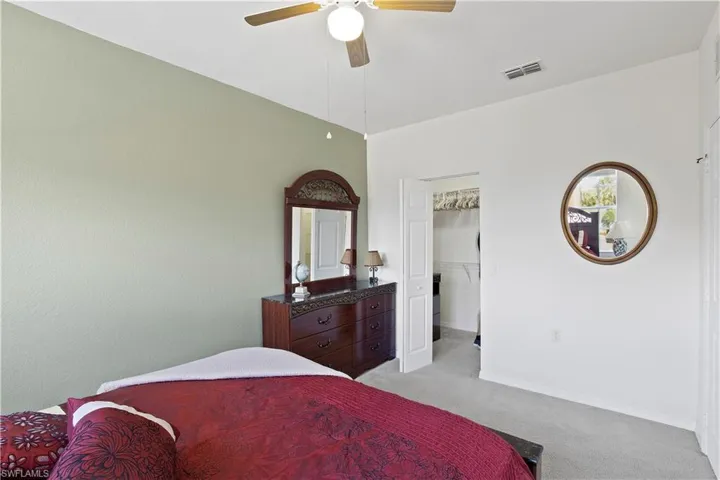 Bedroom featuring light colored carpet, a spacious closet, and ceiling fan