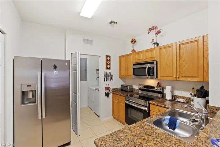 Kitchen featuring stainless steel appliances, washer and clothes dryer, light tile patterned floors, dark countertops, and electric panel