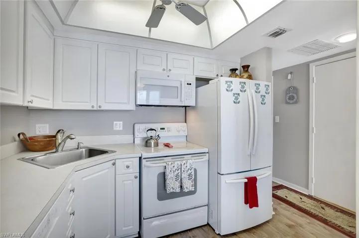Kitchen featuring white appliances, a sink, a ceiling fan, white cabinets, and light countertops