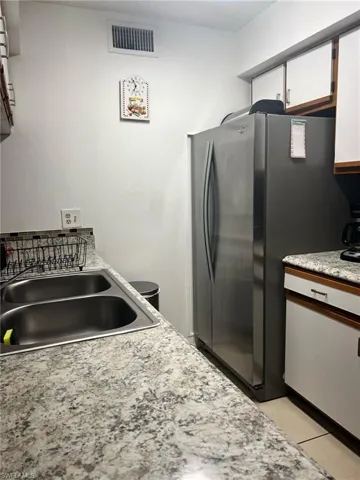 Kitchen featuring freestanding refrigerator, light countertops, white cabinets, and light tile patterned floors