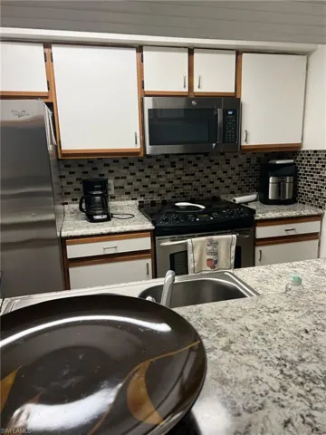 Kitchen with electric range, freestanding refrigerator, decorative backsplash, and white cabinets
