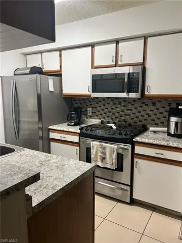 Kitchen featuring appliances with stainless steel finishes, light tile patterned flooring, backsplash, white cabinetry, and a textured ceiling