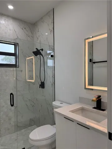 Bathroom with vanity, a shower with shower door, and toilet