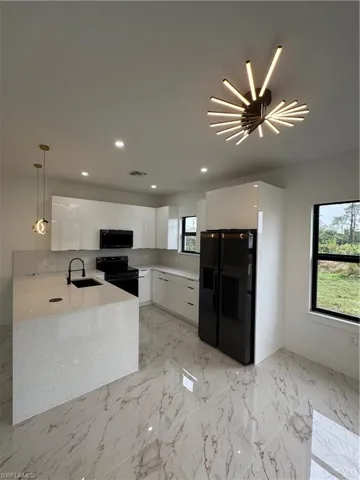 Kitchen with sink, stove, fridge, white cabinets, and decorative light fixtures
