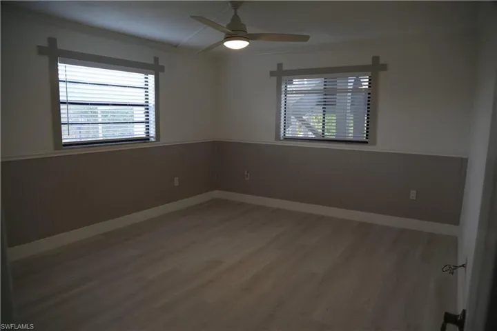 Unfurnished room featuring a wainscoted wall, light wood-type flooring, wooden walls, plenty of natural light, and a ceiling fan