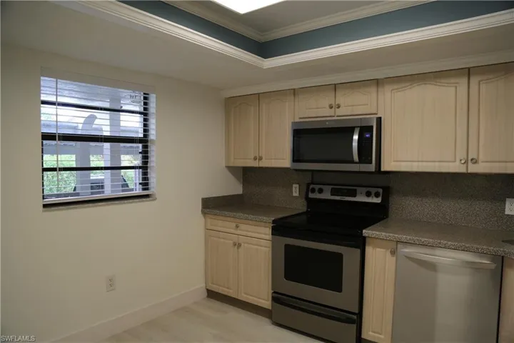 Kitchen featuring stainless steel appliances, ornamental molding, decorative backsplash, light wood finish cabinets, and light wood-style floors