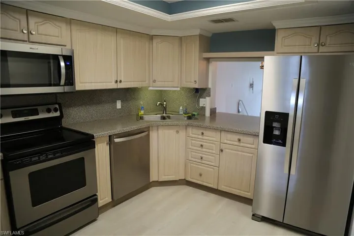 Kitchen featuring stainless steel appliances, decorative backsplash, light wood finish cabinetry, light wood-style flooring, and ornamental molding