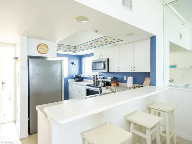 Kitchen with light countertops, white cabinetry, stainless steel appliances, and a breakfast bar