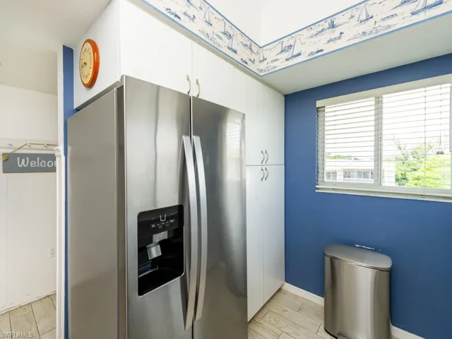 Kitchen with stainless steel refrigerator with ice dispenser, light wood-style flooring, and white cabinets