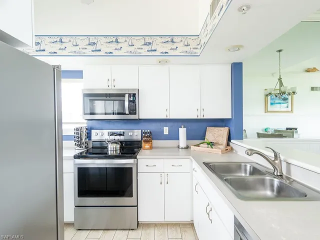 Kitchen with stainless steel appliances, white cabinetry, light countertops, light wood-style flooring, and a chandelier