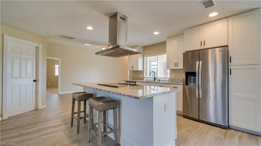 Kitchen with island range hood, stainless steel refrigerator with ice dispenser and white cabinets