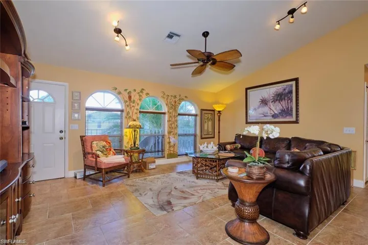Living room featuring rail lighting, ceiling fan, vaulted ceiling, and light tile patterned floors