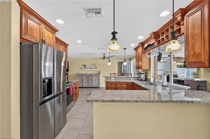 Gourmet kitchen featuring stainless steel appliances, granite countertops, wood cabinetry, recessed lighting, and tile flooring