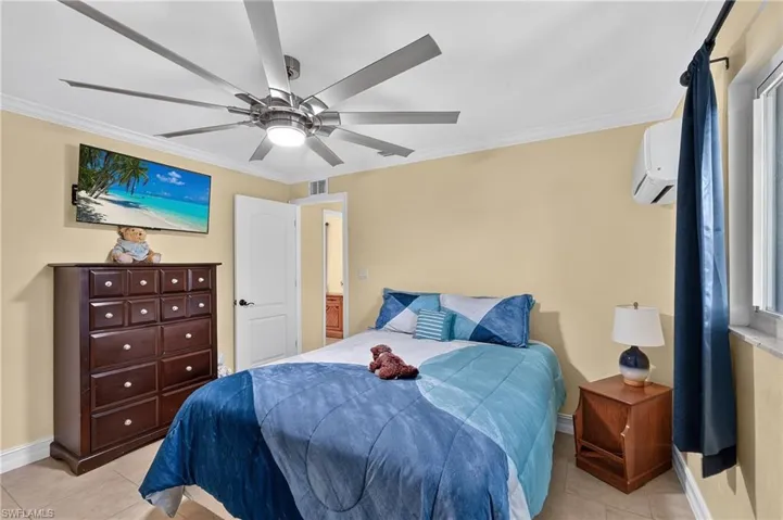 Guest bed #1 Ceiling fan with integrated lighting, wall-mounted television, split air conditioning unit, white paneled door, and tiled flooring