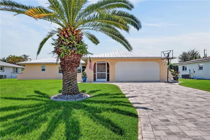 Paver driveway, mature palm tree, manicured lawn, attached garage, arched entry