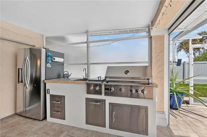 Outdoor kitchen featuring a built-in stainless steel grill, integrated sink, and stainless steel cabinet storage