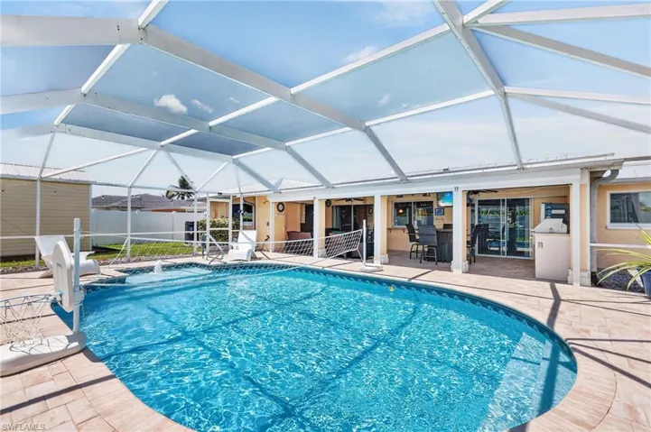 Screened enclosure featuring a curved-edge swimming pool, paver deck, and covered patio with an outdoor bar