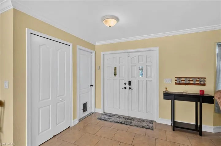 Double entry doors with decorative glass panels, crown molding, and tile flooring