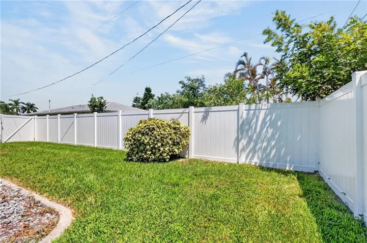 Fenced and Expansive backyard featuring a manicured lawn, white privacy fencing, and mature landscaping