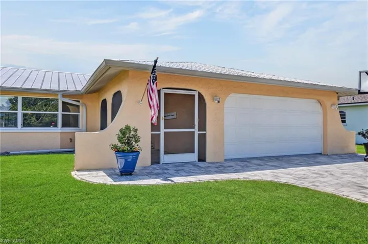 Stucco exterior with a metal roof, paver driveway, and a screened entry