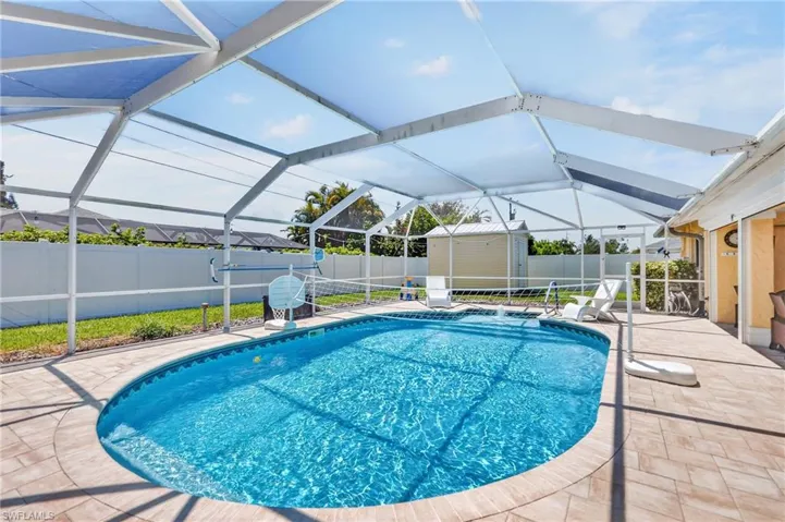 Screened pool enclosure with a freeform swimming pool, paver deck, and a white privacy fence