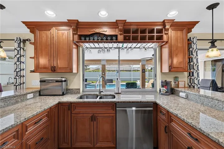 U-shaped kitchen with granite countertops, wood cabinetry, stainless steel double basin sink, and a pass-through window with a wine glass rack