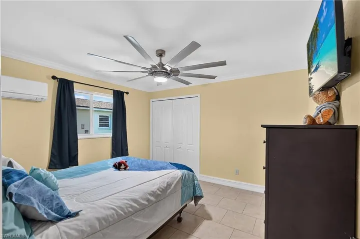 Guest Bed#1 Ceiling fan with integrated lighting, tiled flooring, built-in closet with bi-fold doors, crown molding, and a wall-mounted air conditioning unit